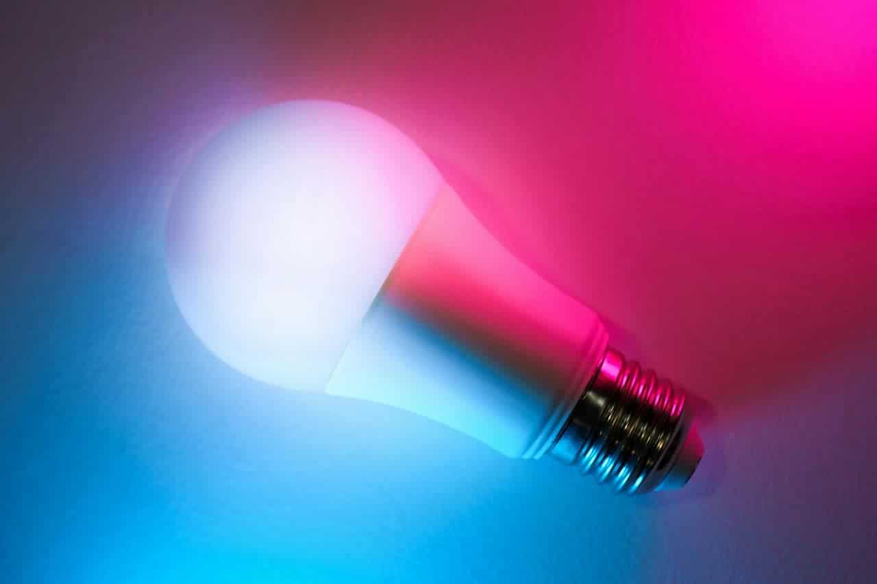 Illuminated LED light bulb with glowing white globe emitting blue and pink light against gradient background