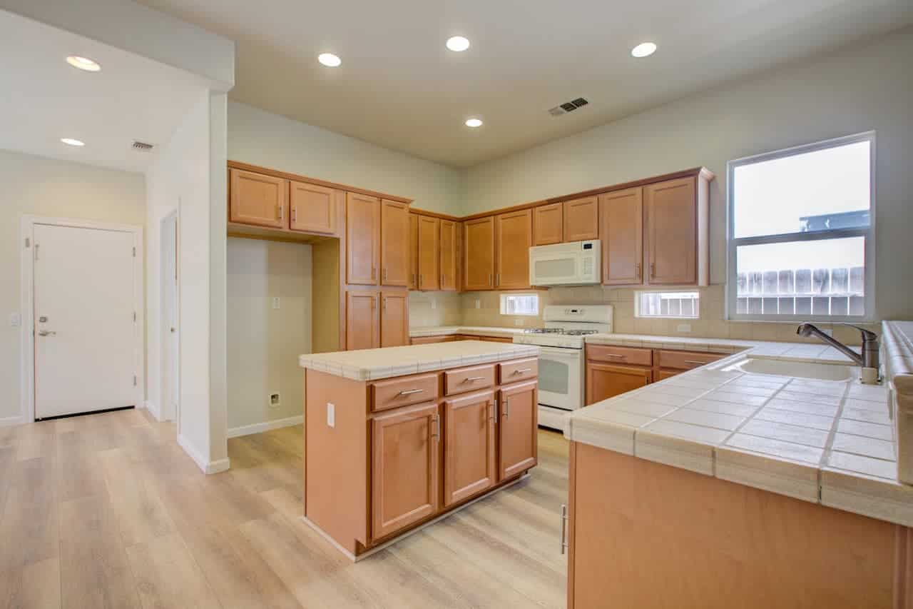 Modern kitchen with light wood cabinets, white appliances, tile countertops, central island, and wood-look flooring