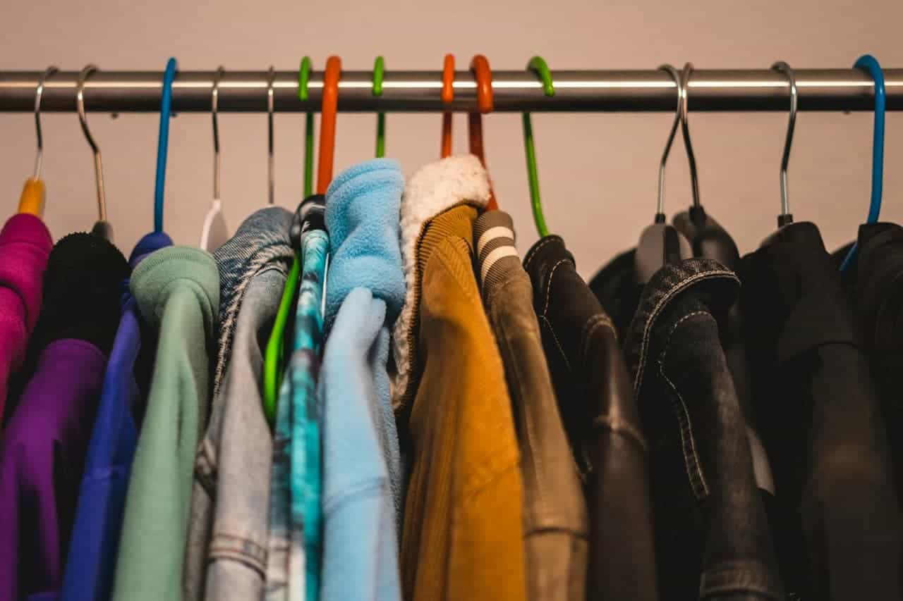Clothing rack with various garments hanging on colorful hangers, including bright and dark colored shirts, sweaters, and jackets