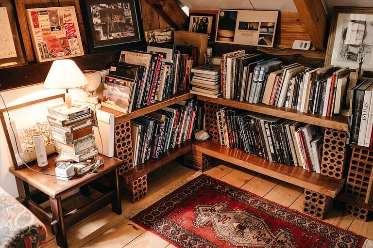 Cozy reading nook with wooden bookshelves made from cinder blocks, filled with books, featuring a red patterned rug and lamp
