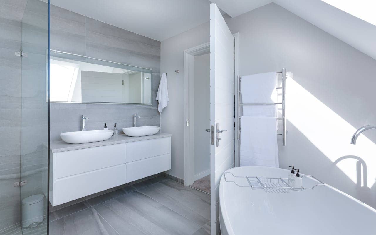 Modern white bathroom with dual vessel sinks, floating vanity, freestanding tub, glass shower enclosure, and heated towel rack