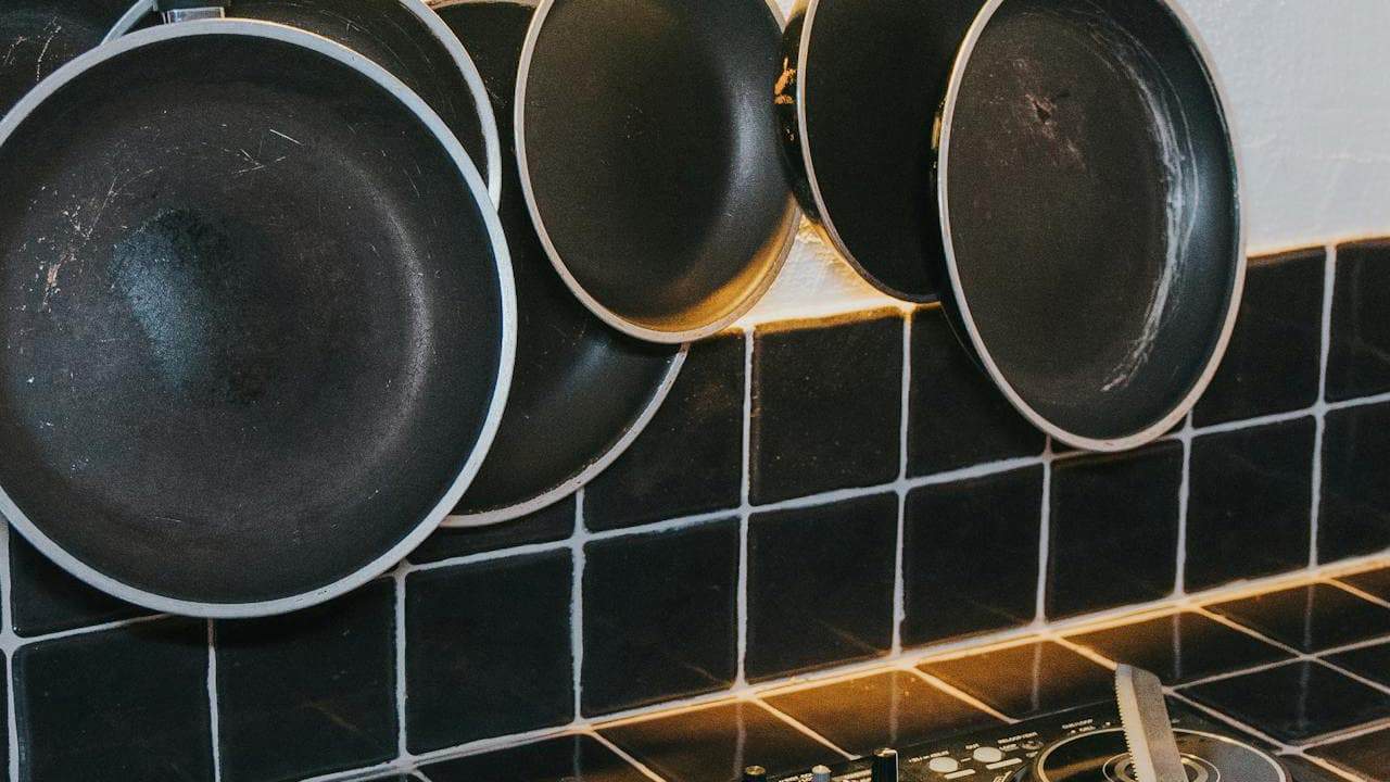 Black non-stick frying pans with light-colored rims stacked and stored on dark green subway tile kitchen backsplash
