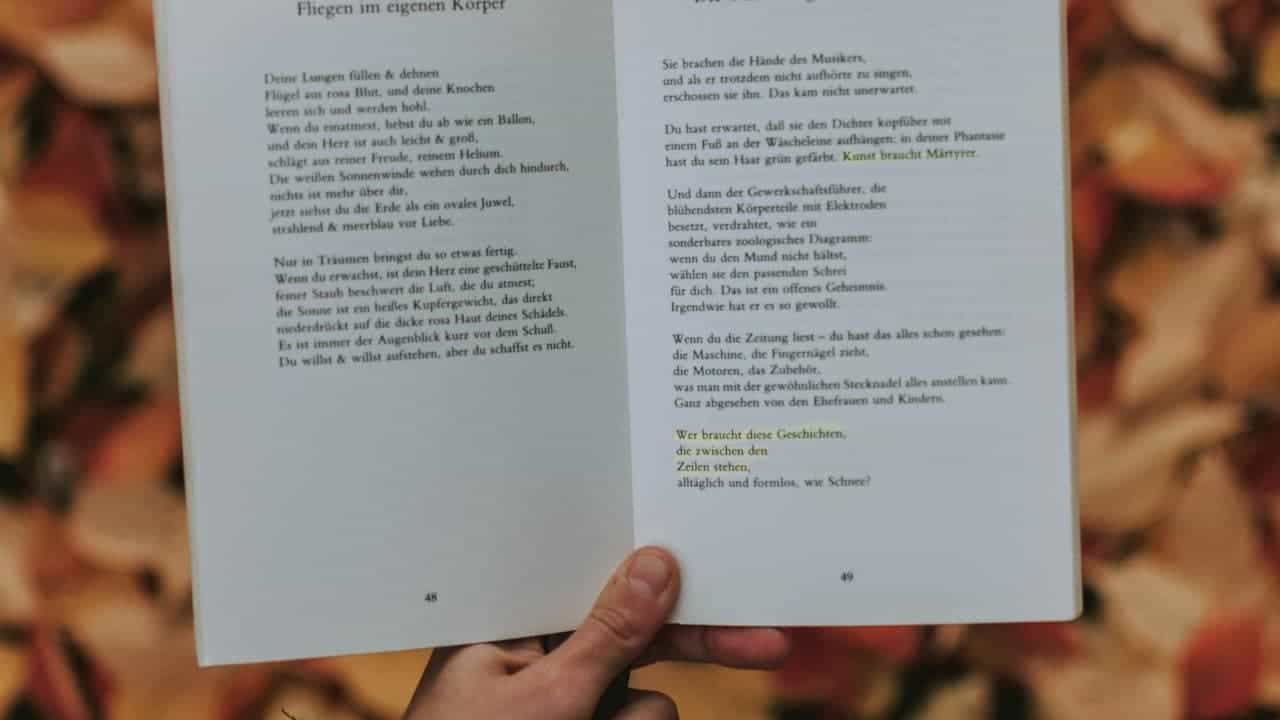 Hand holding open German poetry book showing pages 48-49 with poem titled "Fliegen im eigenen Körper" against blurred background