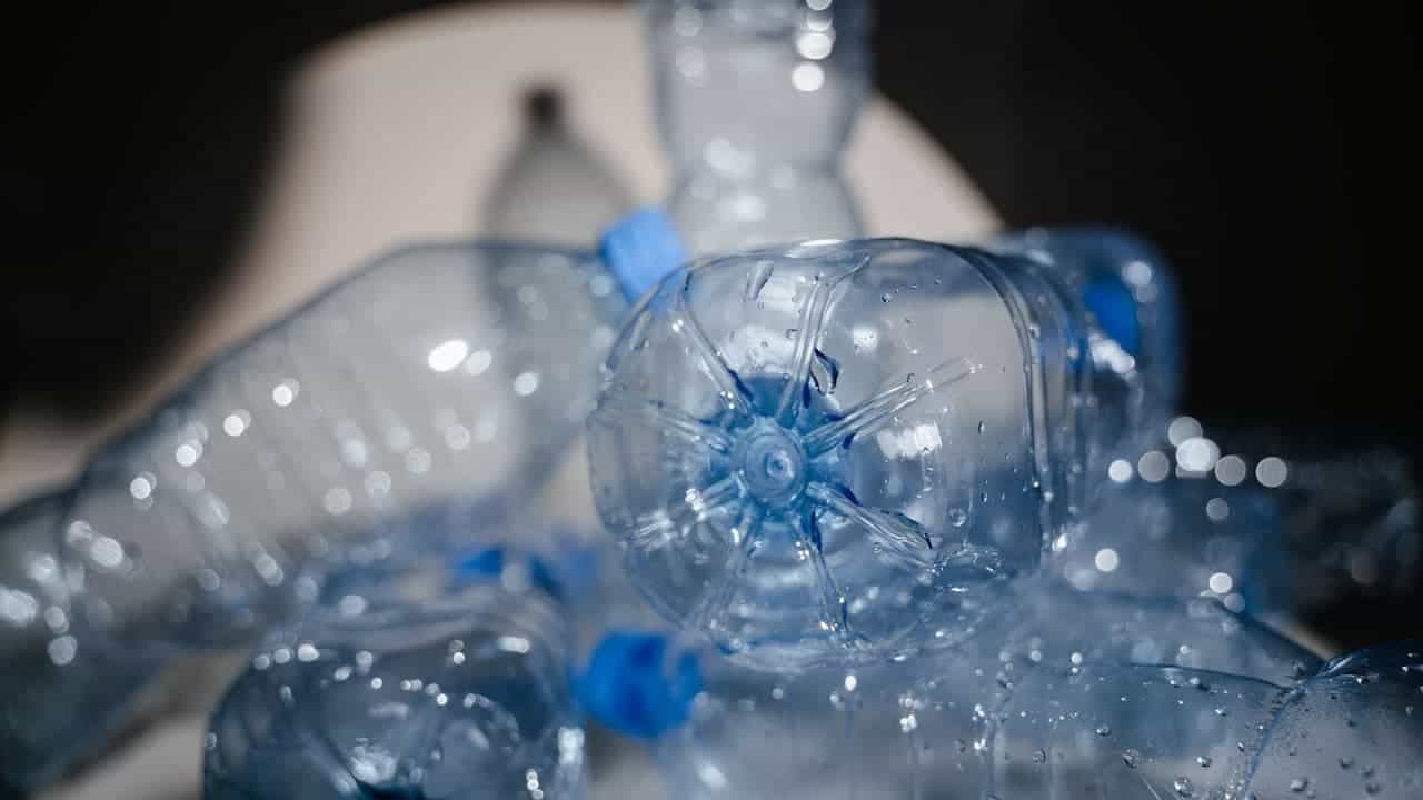 Close-up of clear plastic water bottles with blue caps scattered together, showing water droplets and reflective light bokeh effects