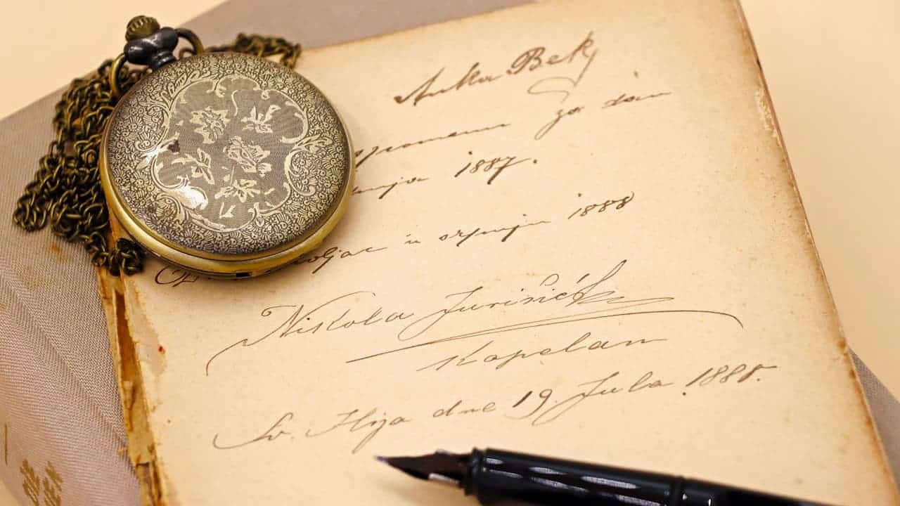 Antique pocket watch with ornate floral engravings on gold chain, resting on aged handwritten letter with fountain pen nearby