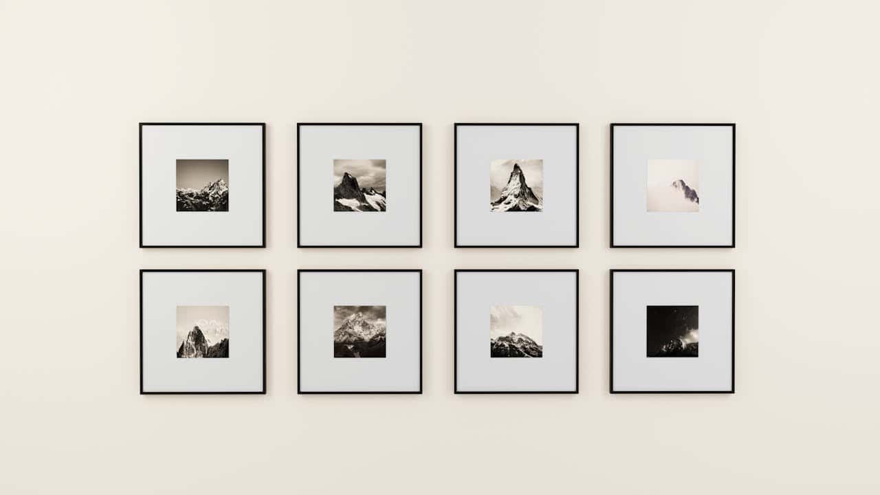 Eight framed black-and-white art prints arranged in two rows on a minimalist white wall, featuring dramatic alpine peaks