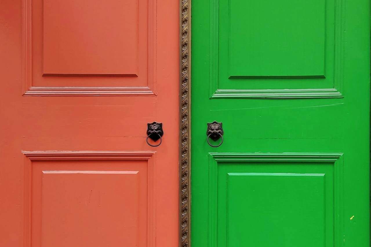 Adjacent coral-orange and bright green doors with identical decorative lion head knockers, separated by ornate carved trim