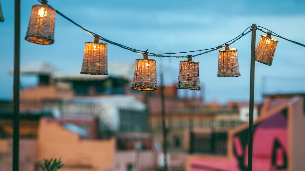 Woven basket solar lanterns hanging above blurred urban rooftops, creating warm ambiance against blue evening sky