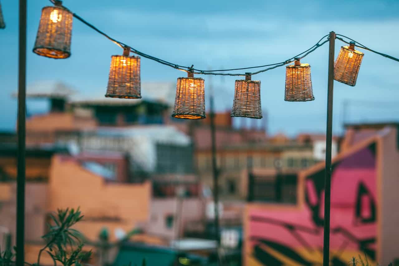 Woven basket solar lanterns hanging above blurred urban rooftops, creating warm ambiance against blue evening sky