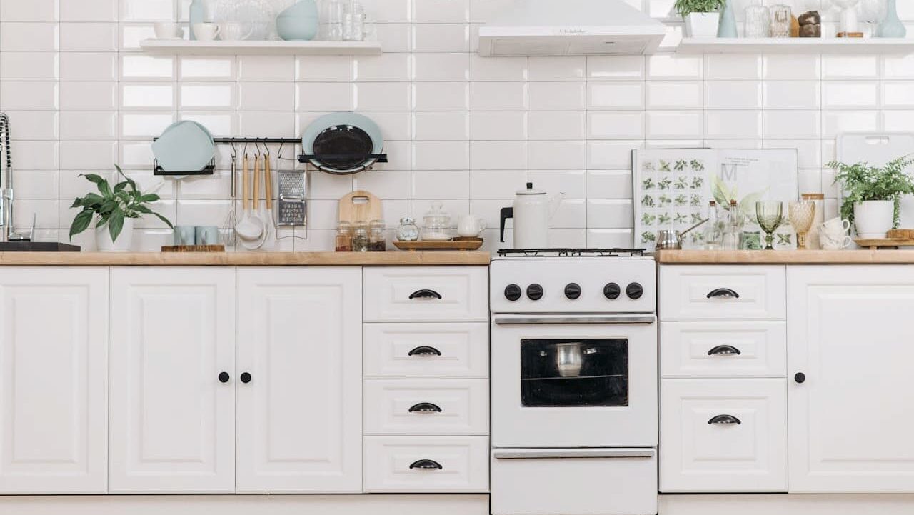 White kitchen with subway tile backsplash, wooden countertops, white stove, cabinets with black handles, and mint accents