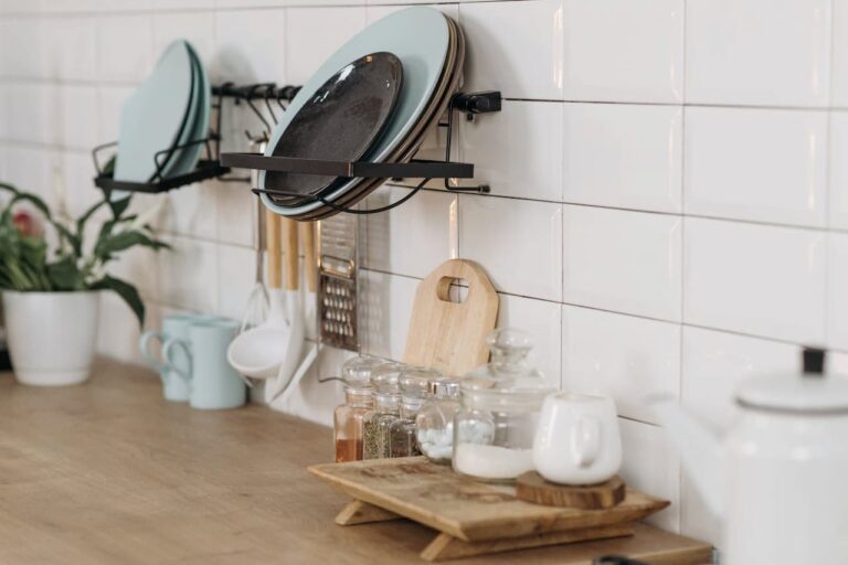 Modern kitchen corner with wall-mounted plate rack, wooden counter displaying spice jars, and minimalist white-tiled backsplash