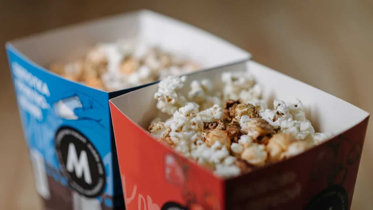 Two cardboard popcorn containers side by side, one blue and one red, filled with white and caramel popcorn