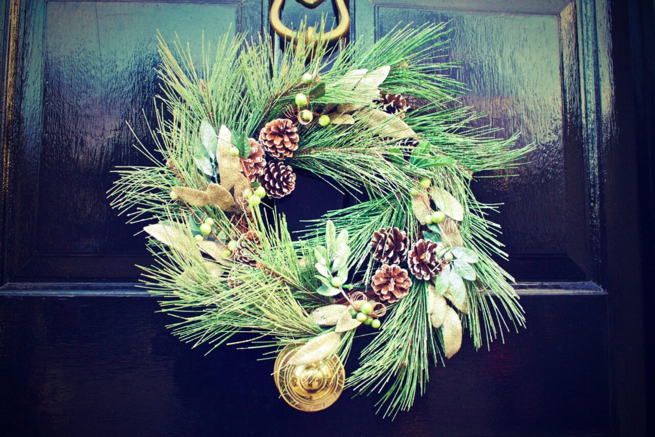 Wreath with pine needles, pinecones, gold leaves, and green berries, hanging on a glossy black front door