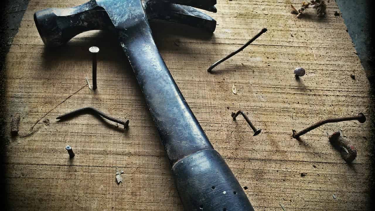 Dark-colored hammer with a wooden or black handle, close-up view on a dark background