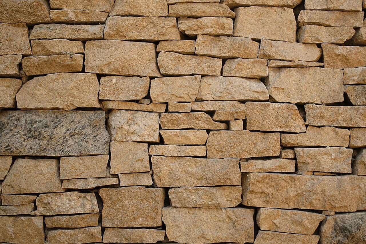 Textured stone wall with irregular golden-brown rocks carefully stacked, creating intricate pattern of varying sizes and natural textures