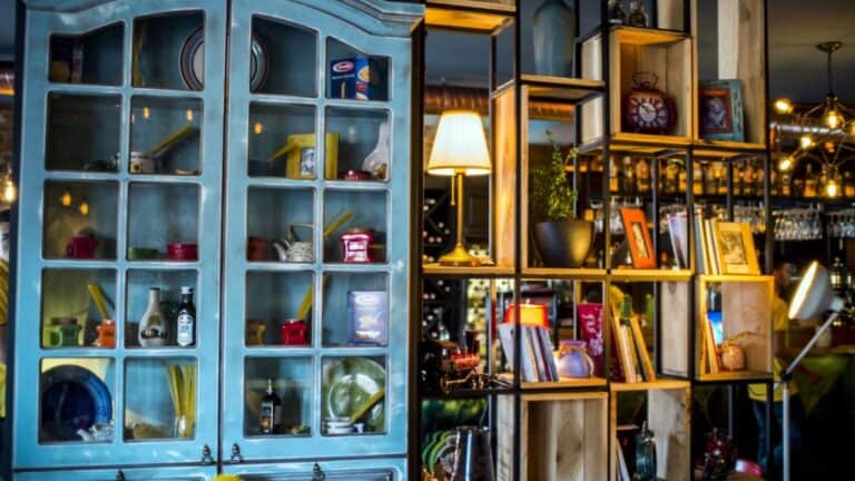 Vintage blue cabinet with glass doors displaying collectibles next to wooden cube shelving filled with books, lamps, and decorative items