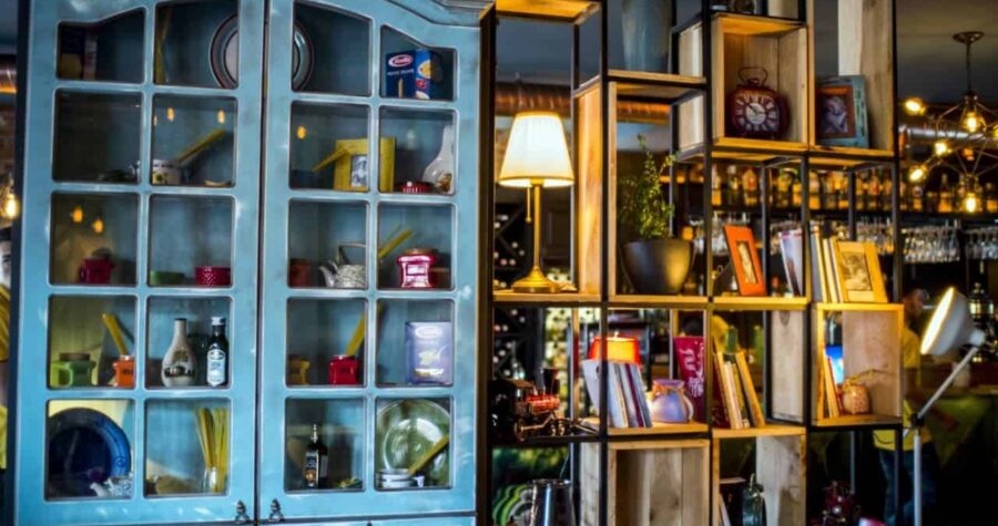 Vintage blue cabinet with glass doors displaying collectibles next to wooden cube shelving filled with books, lamps, and decorative items