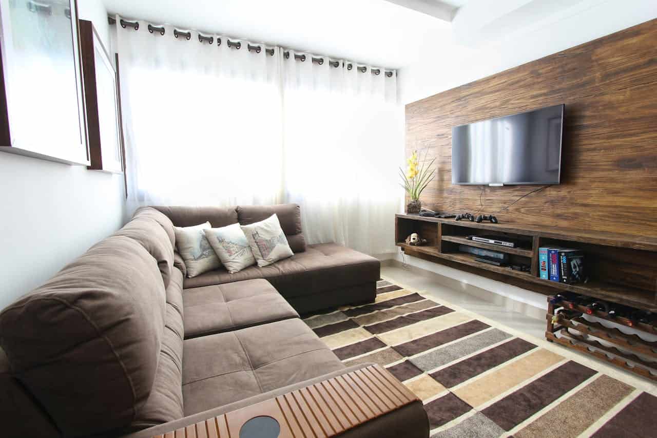 Modern living room with brown sectional sofa, wall-mounted TV, wood panel wall, striped rug, and floating entertainment shelf