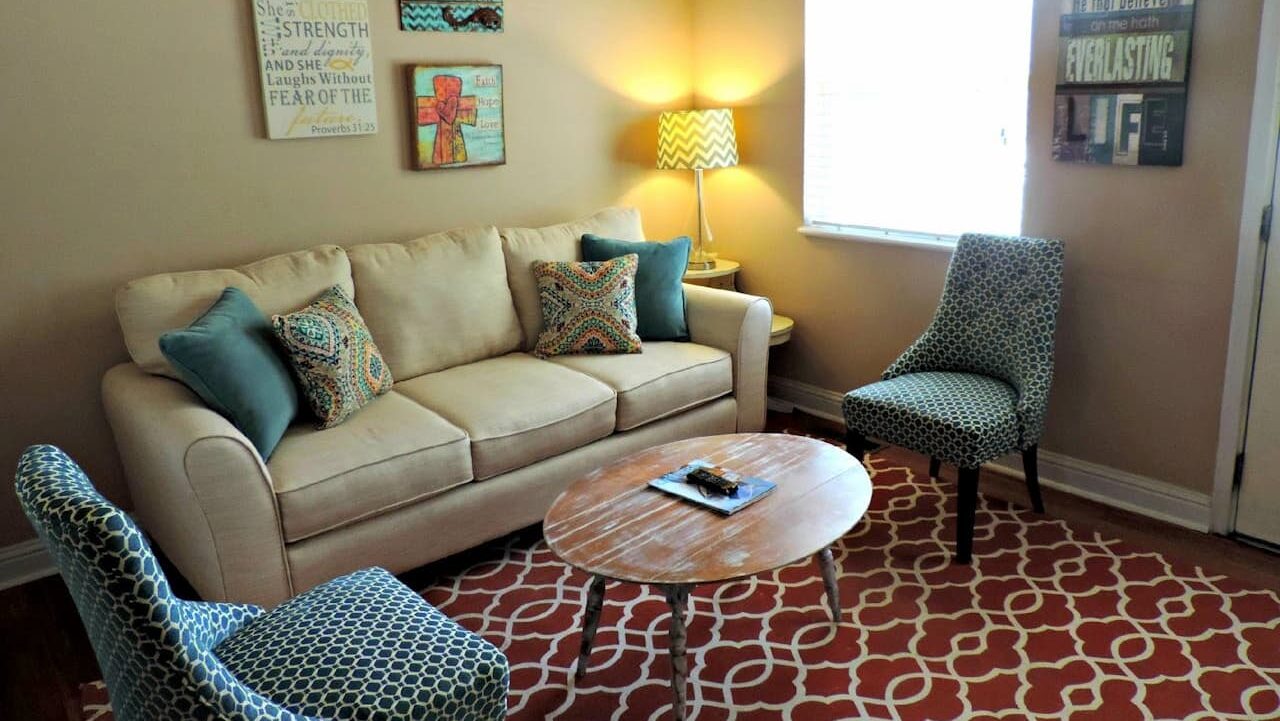 Cozy living room with beige sofa, blue accent chairs, wooden coffee table, patterned rug, and religious wall art