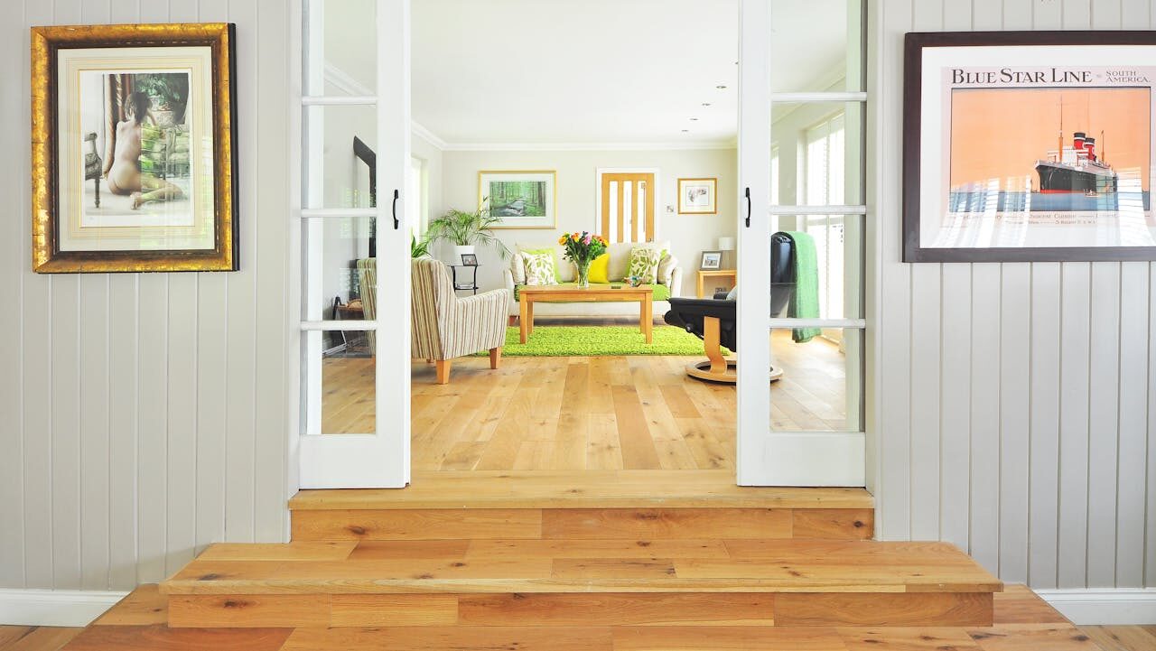 Sliding barn doors opening to bright living room with wooden floors, green rug, and framed artwork on surrounding walls