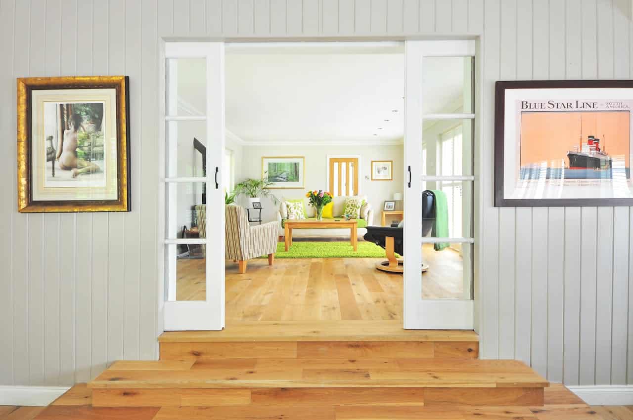 Sliding barn doors opening to bright living room with wooden floors, green rug, and framed artwork on surrounding walls
