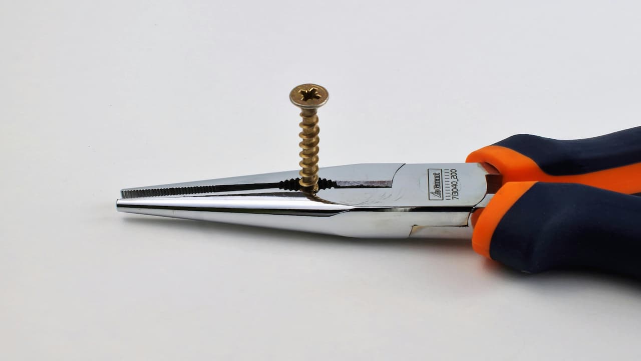 Pliers gripping a small screw firmly, close-up view, metal tools, mechanical setting