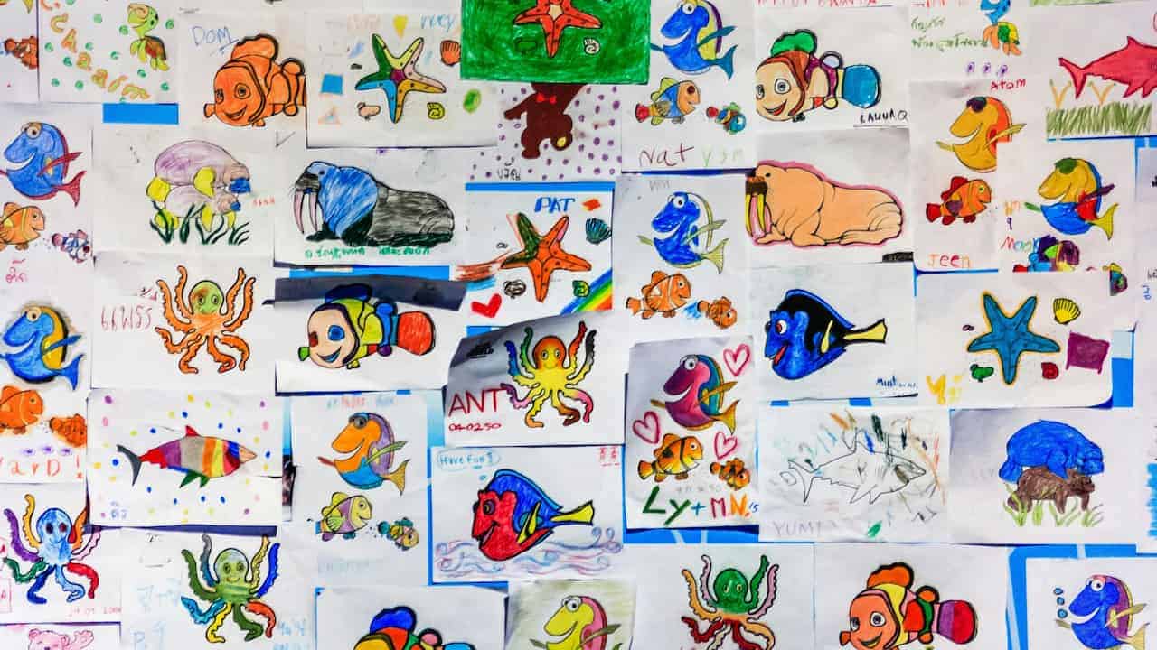 A wall covered with colorful children's drawings of marine animals, including fish, octopuses, starfish, and other sea creatures