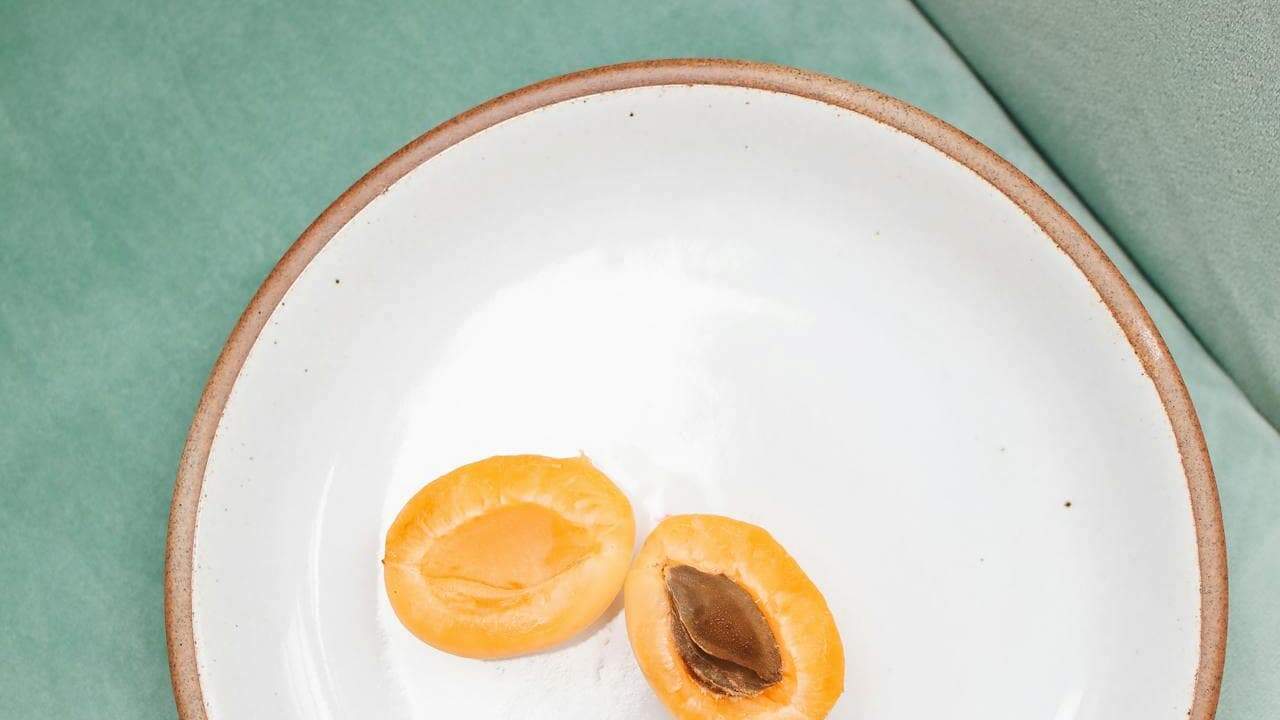 Two halved apricots on a white ceramic plate with brown rim, placed on mint green surface
