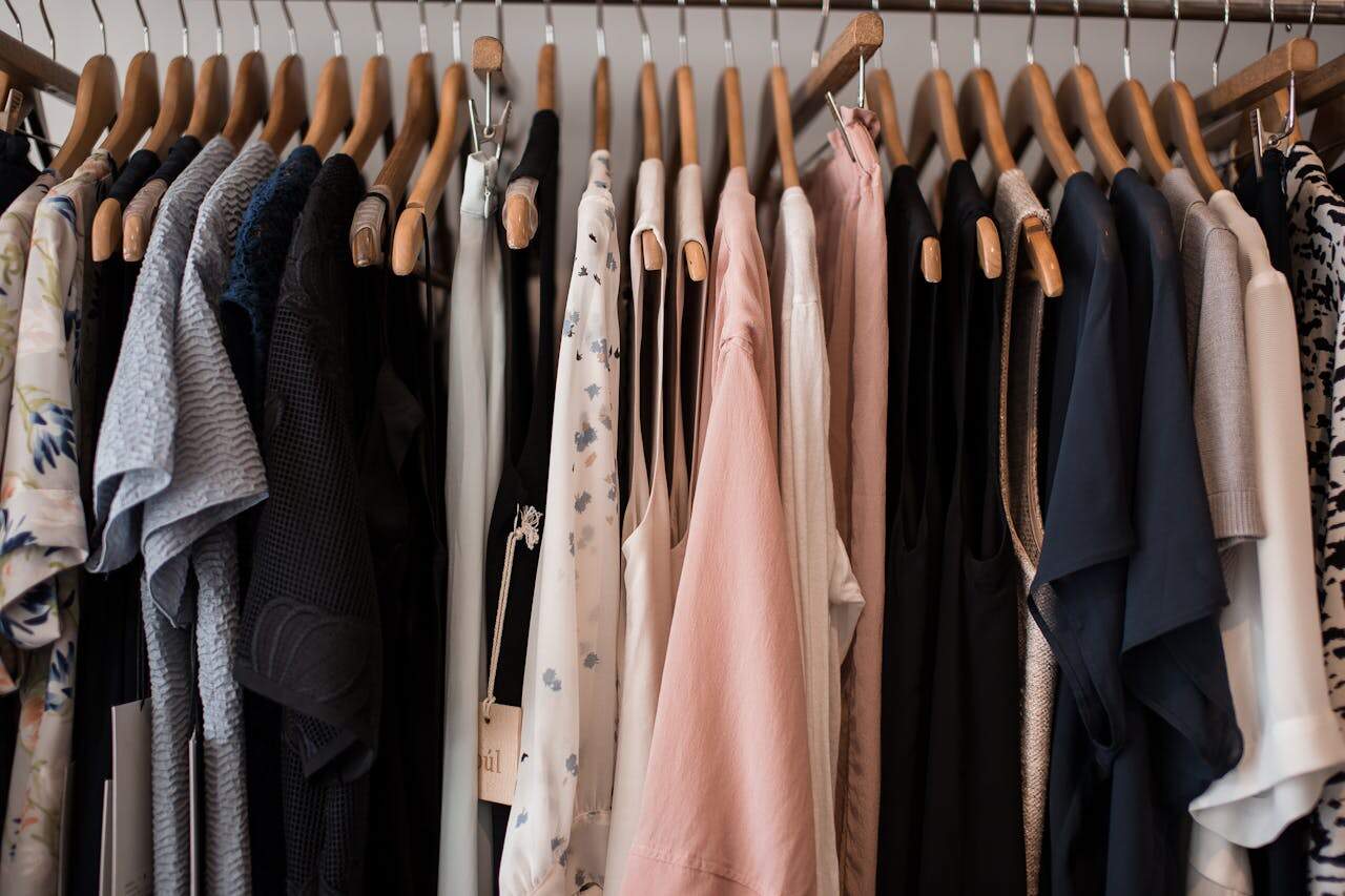 Clothing rack with wooden hangers displaying an organized collection of garments in neutral colors, pastels, and patterns