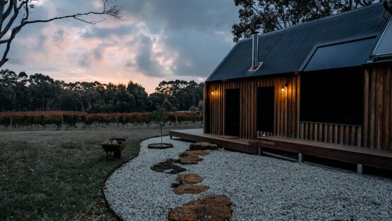 Wooden cabin with metal roof beside gravel garden path with flexible steel edging, overlooking vineyard at sunset with dramatic cloudy sky