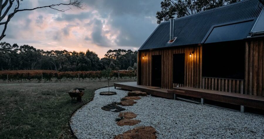 Wooden cabin with metal roof beside gravel garden path with flexible steel edging, overlooking vineyard at sunset with dramatic cloudy sky