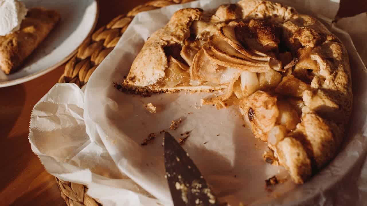 German Apple Cake with golden crust on parchment paper, with one slice removed, served on woven placemat