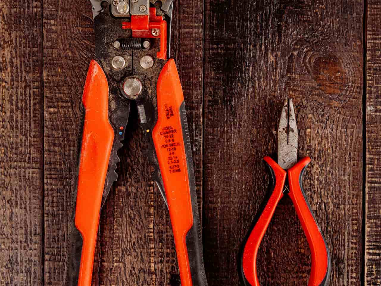 Wire stripper and pliers placed side by side, metal jaws and insulated handles visible, tools for electrical work