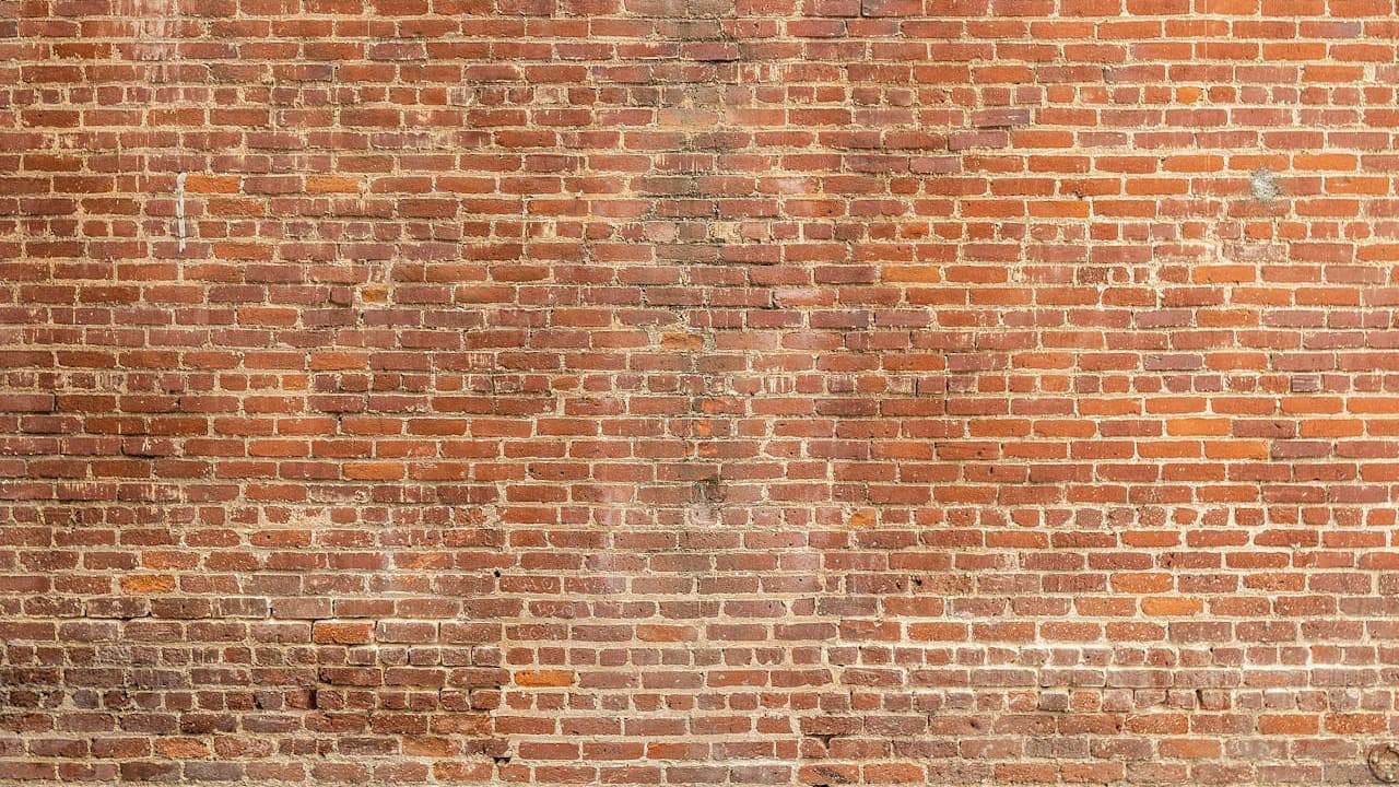 Weathered red brick wall with white mortar joints showing age, discoloration, and surface wear across the masonry surface