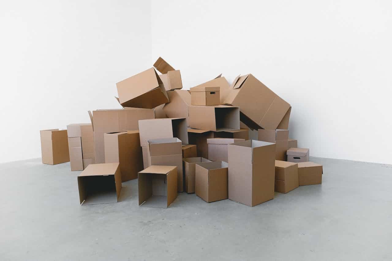 Large pile of empty cardboard boxes in various sizes stacked haphazardly on concrete floor against white wall