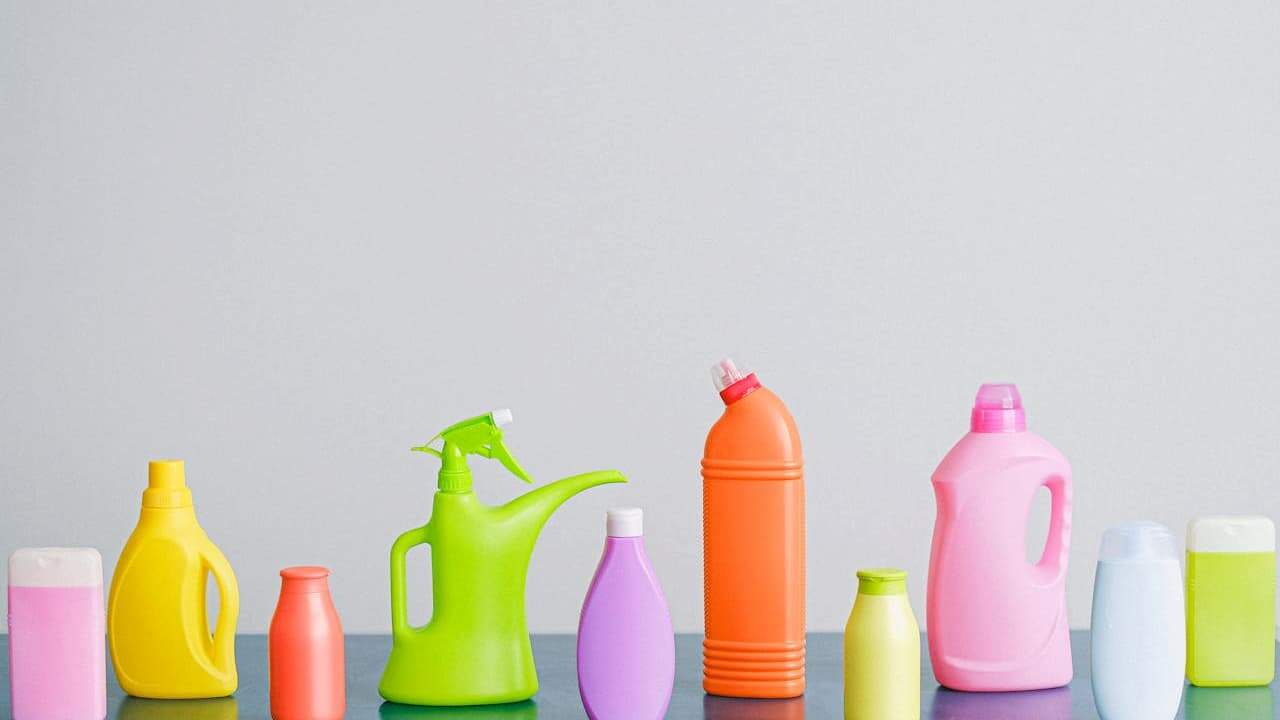A row of colorful plastic cleaning bottles of various shapes and sizes, including spray bottles and detergent containers