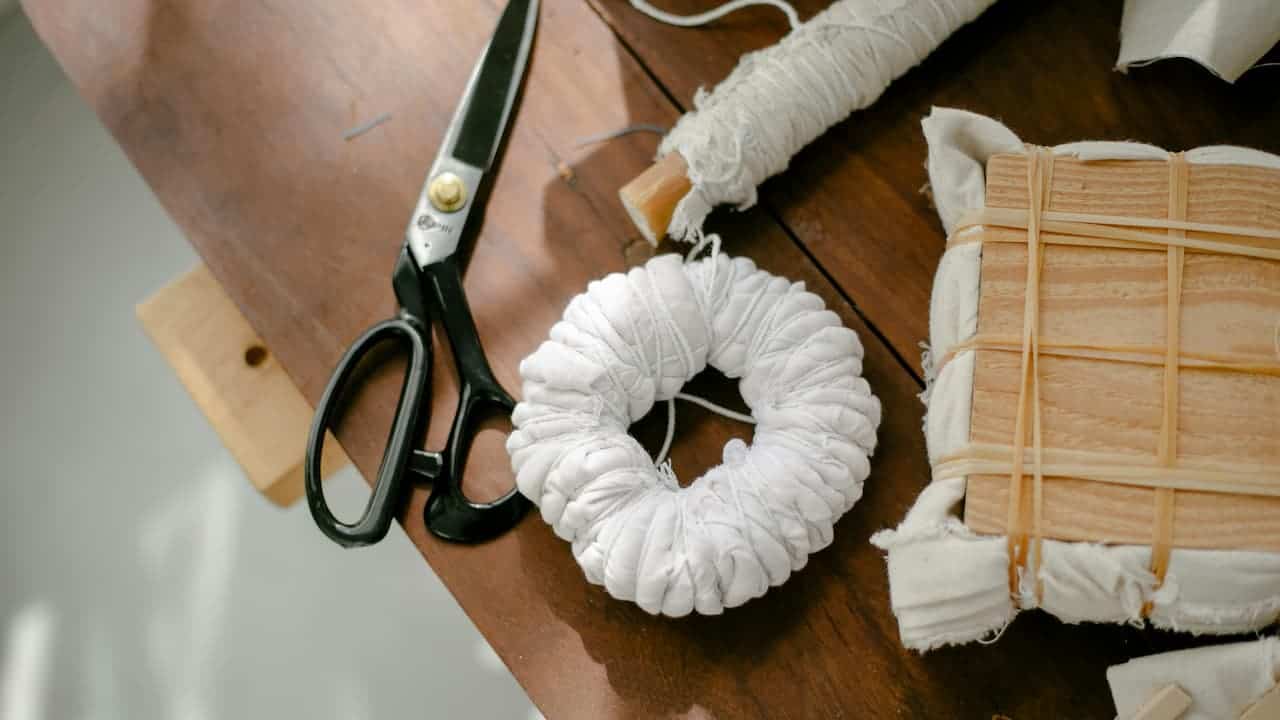 Black Panasonic scissors on wooden surface with white fabric scrunchie, wrapped cord, and wooden craft supplies for sewing project