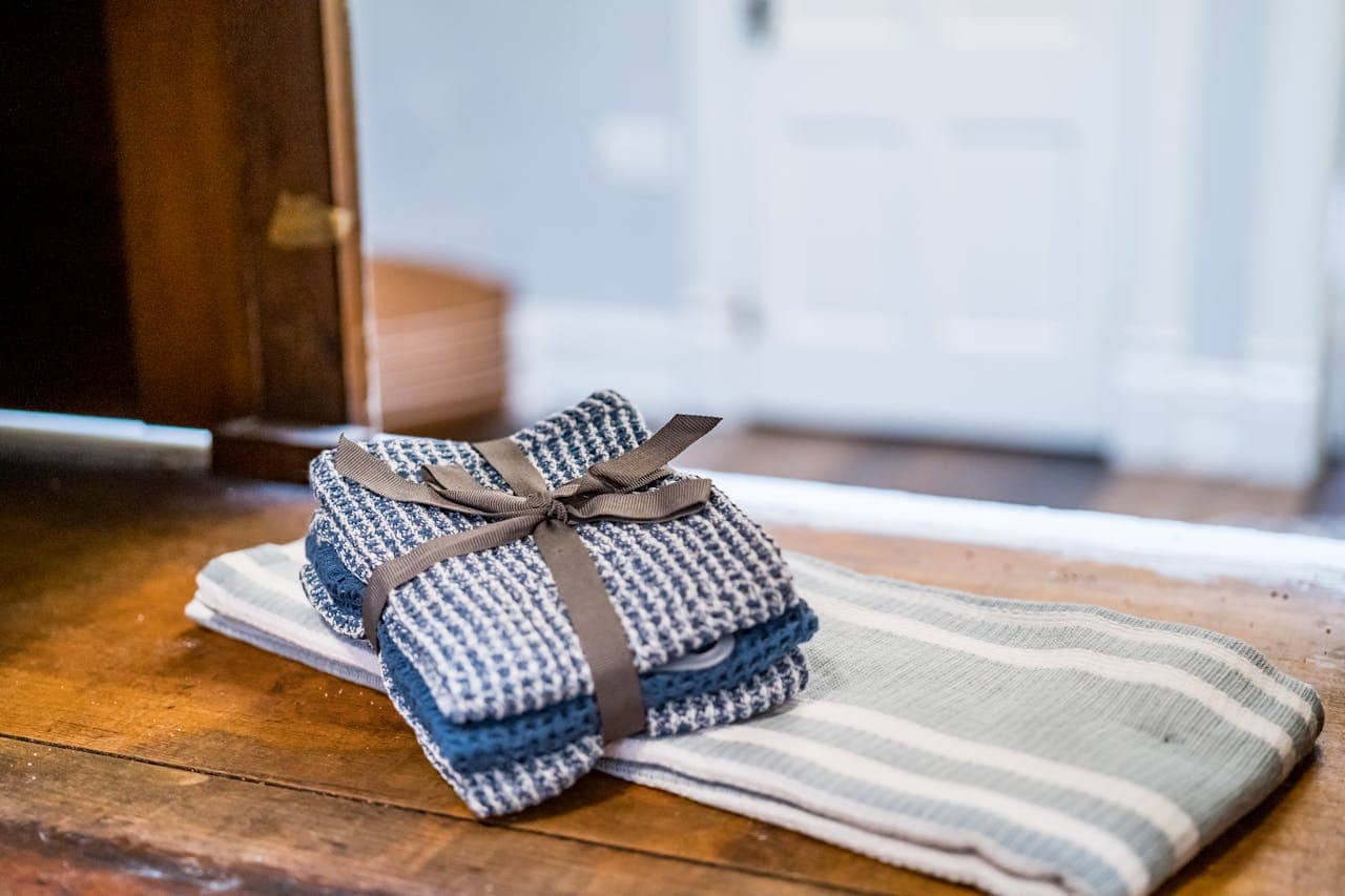 Stack of folded blue and white kitchen towels tied with brown ribbon, placed on striped cloth on wooden table