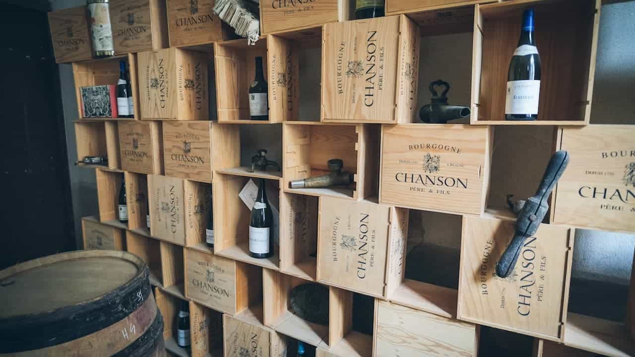 Wooden wine crates used as shelves holding wine bottles, vintage tools, and decor items, with a wine barrel in foreground