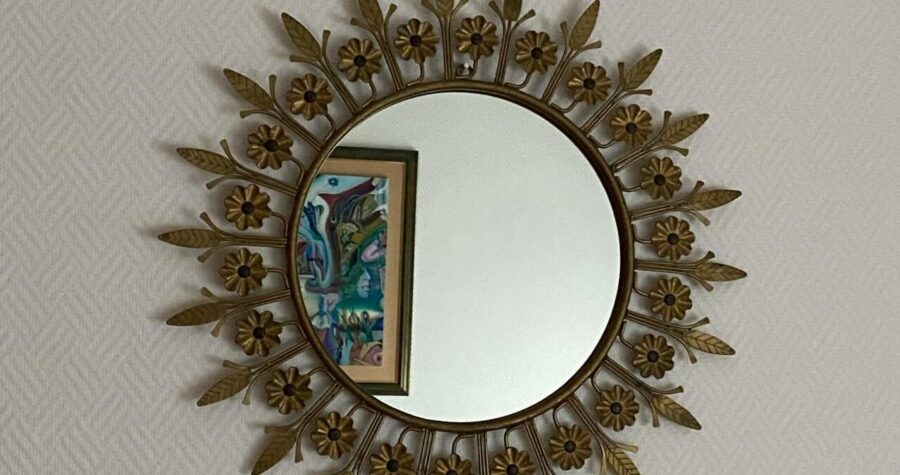 Round mirror with decorative brass sunburst frame featuring flower and leaf details, mounted on textured white wall