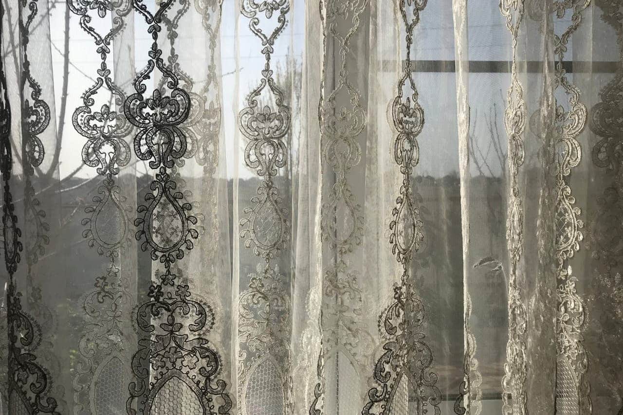 Translucent sheer curtains curtains with ornate embroidered patterns filtering daylight through a window, creating soft shadows and silhouettes