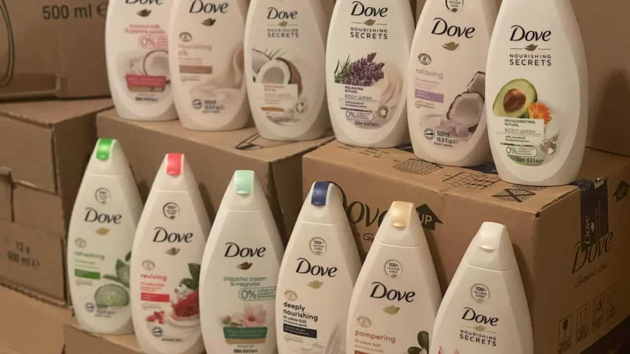 Multiple Dove body wash bottles arranged on cardboard boxes, featuring various scents including coconut, lavender, and avocado in white packaging