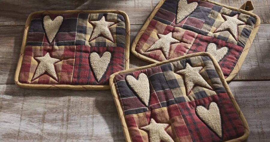 Three handmade tattered pot holders with plaid fabric and burlap heart and star appliques on weathered wooden surface