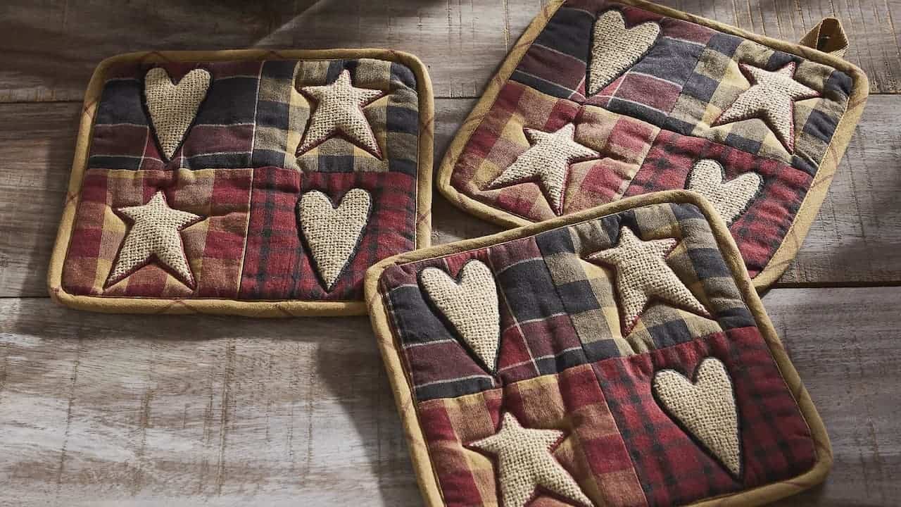 Three handmade tattered pot holders with plaid fabric and burlap heart and star appliques on weathered wooden surface