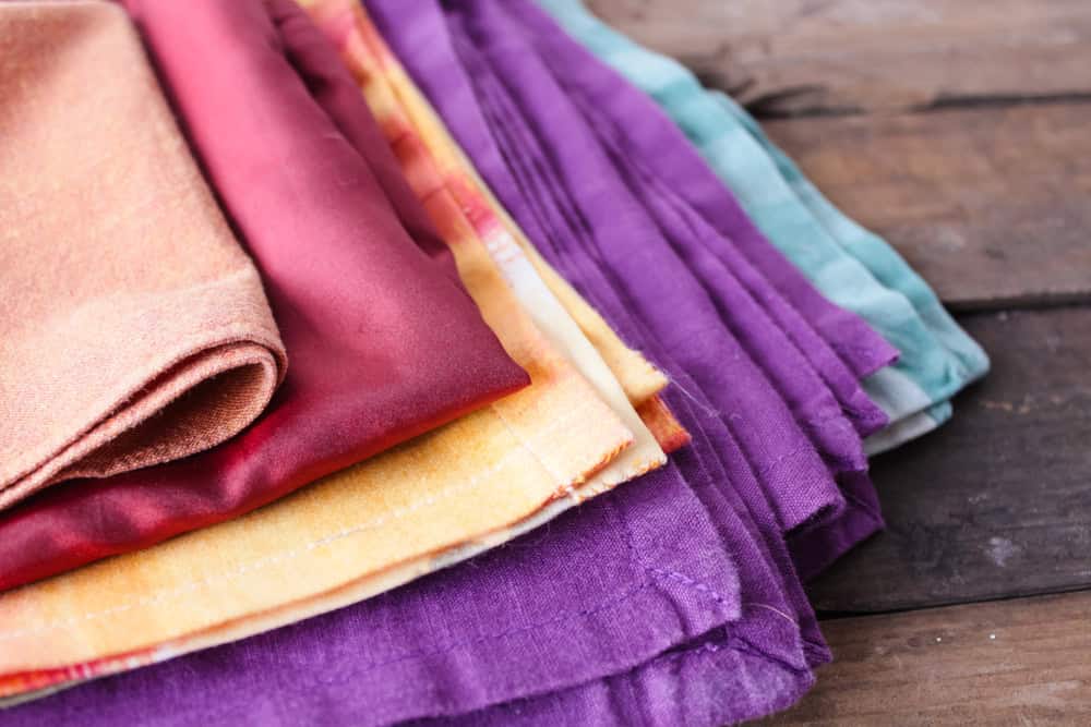 Stack of colorful folded fabric pieces in shades of purple, yellow, red, orange, and teal, placed on a rustic wooden surface