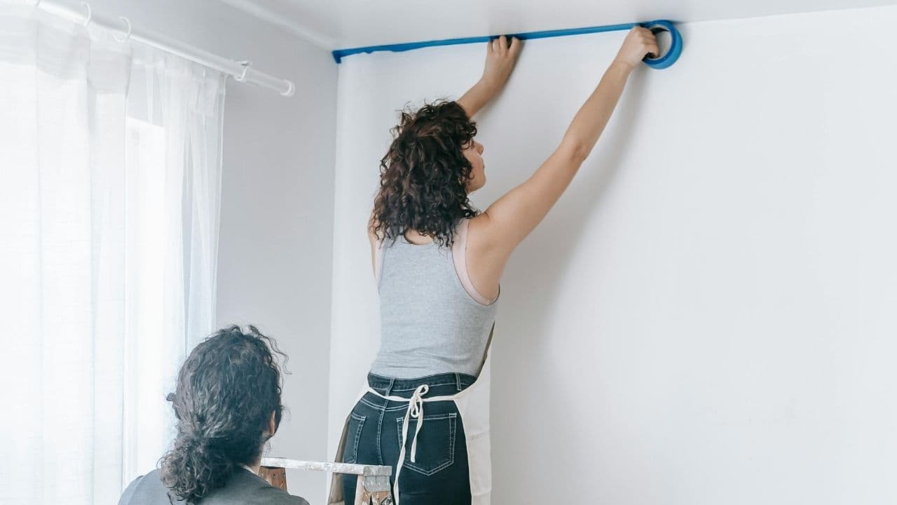 Hand applying blue painter’s tape to a smooth surface, close-up view, preparing area for painting