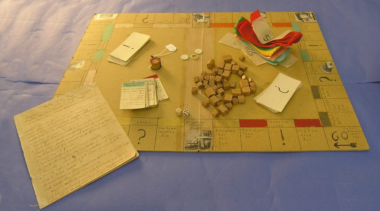 Vintage 1930s Monopoly board game with wooden houses, cards, dice, and handwritten rules on blue surface