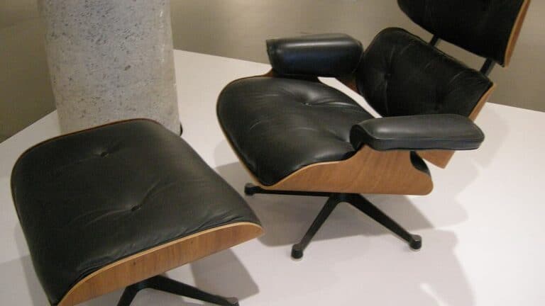 Mid-century modern Eames lounge chair and ottoman in black leather with wood frame on white surface