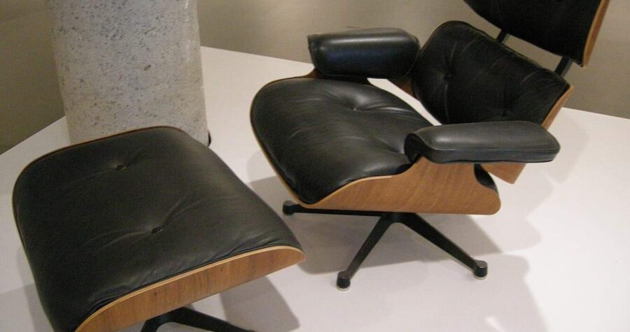 Mid-century modern Eames lounge chair and ottoman in black leather with wood frame on white surface