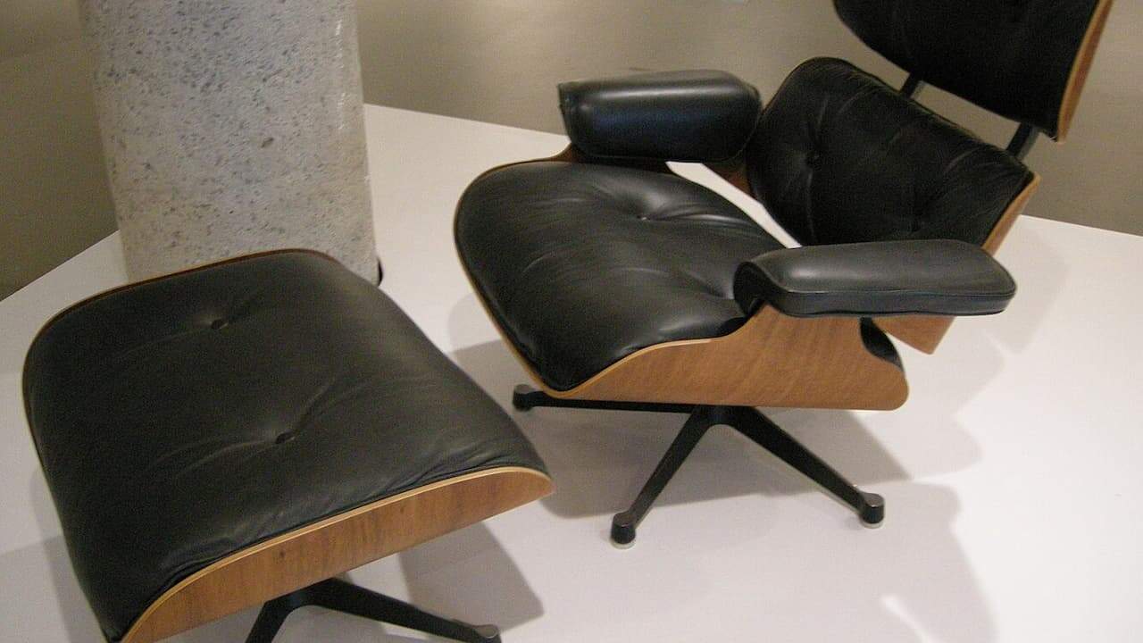 Mid-century modern Eames lounge chair and ottoman in black leather with wood frame on white surface